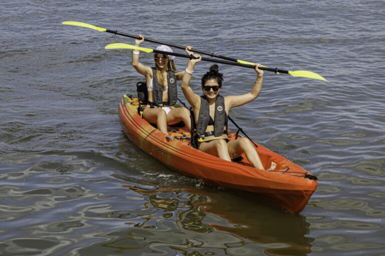 three people in a kayak with paddles on the water