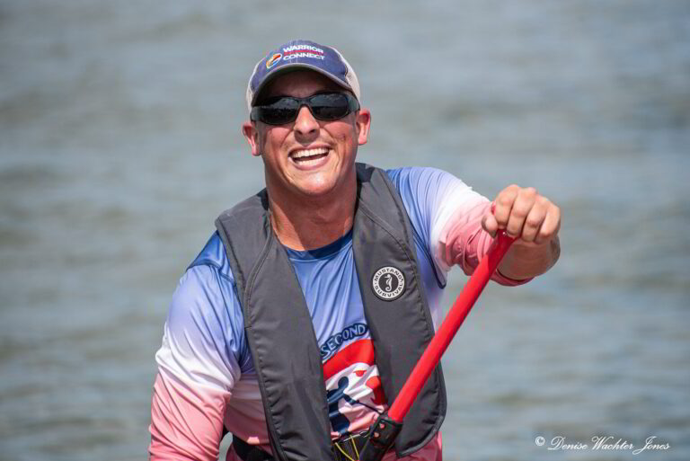 a man in a life jacket smiles while holding a paddle