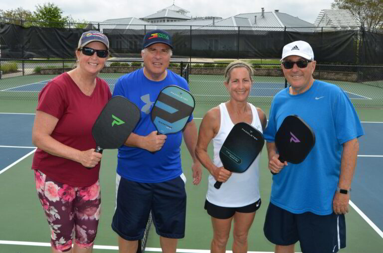 four people standing on a tennis court holding racquets