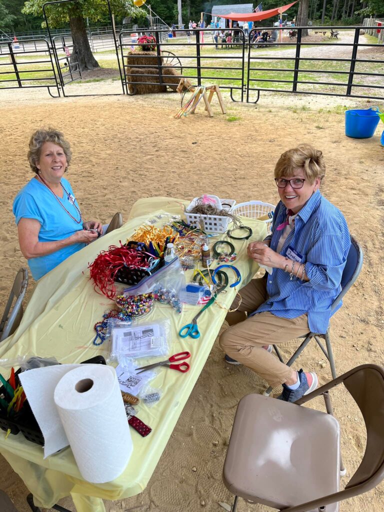 two women sitting at a table covered in craft supplies