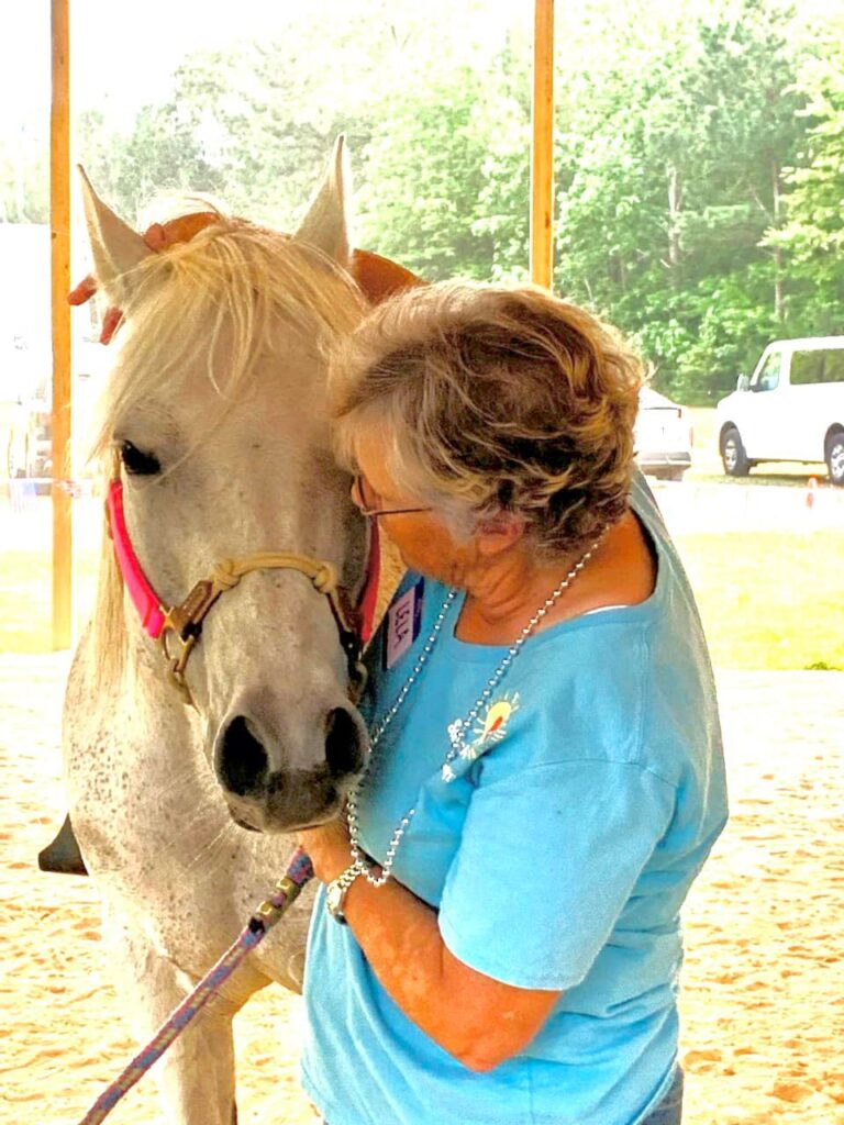 a woman in blue shirt petting a white horse