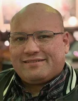 a bald man wearing glasses and a green jacket